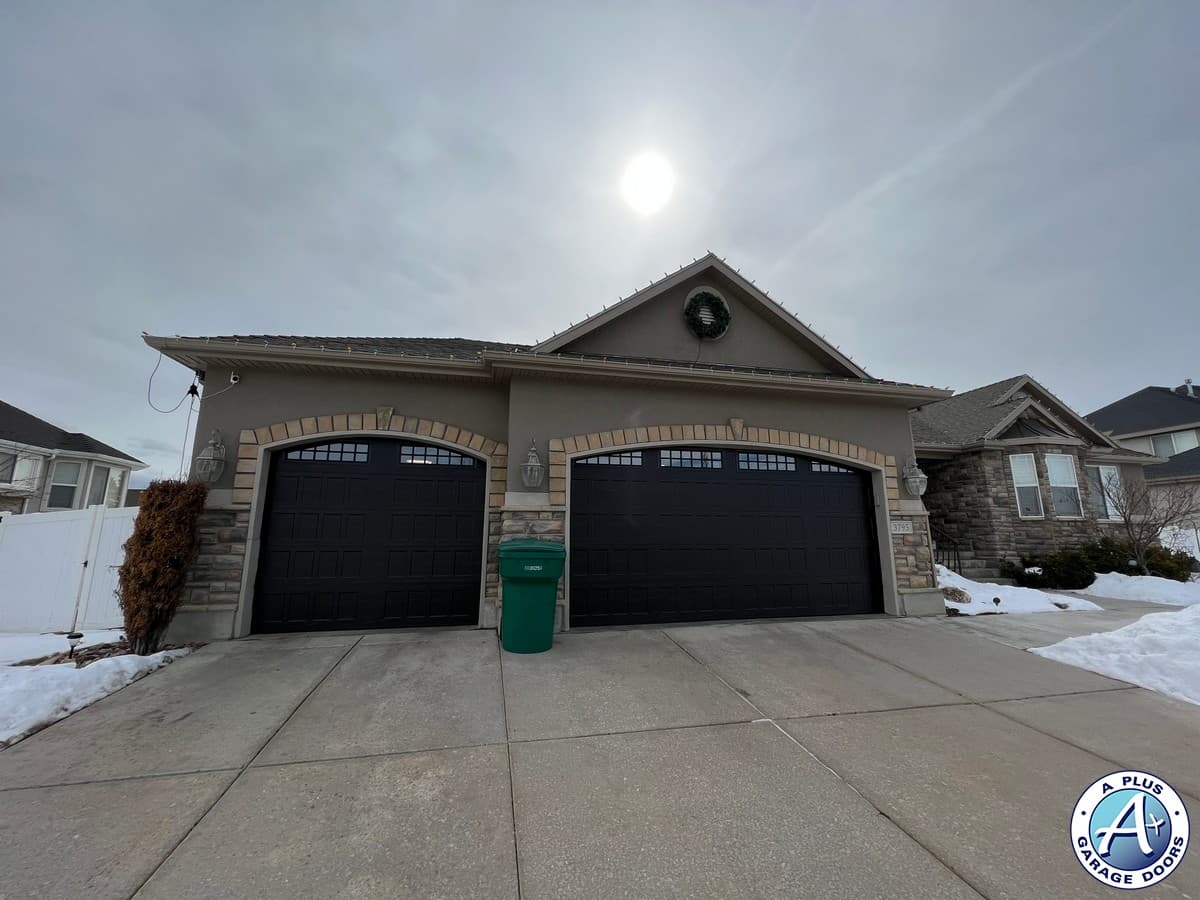 A black traditional long-panel insulated garage door installed on a residential home in Roy, Utah.