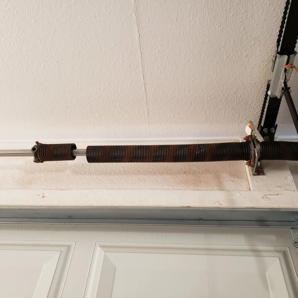 Heavy rust on torsion springs mounted above a garage door — the surface corrosion you want to catch before the first cold morning.